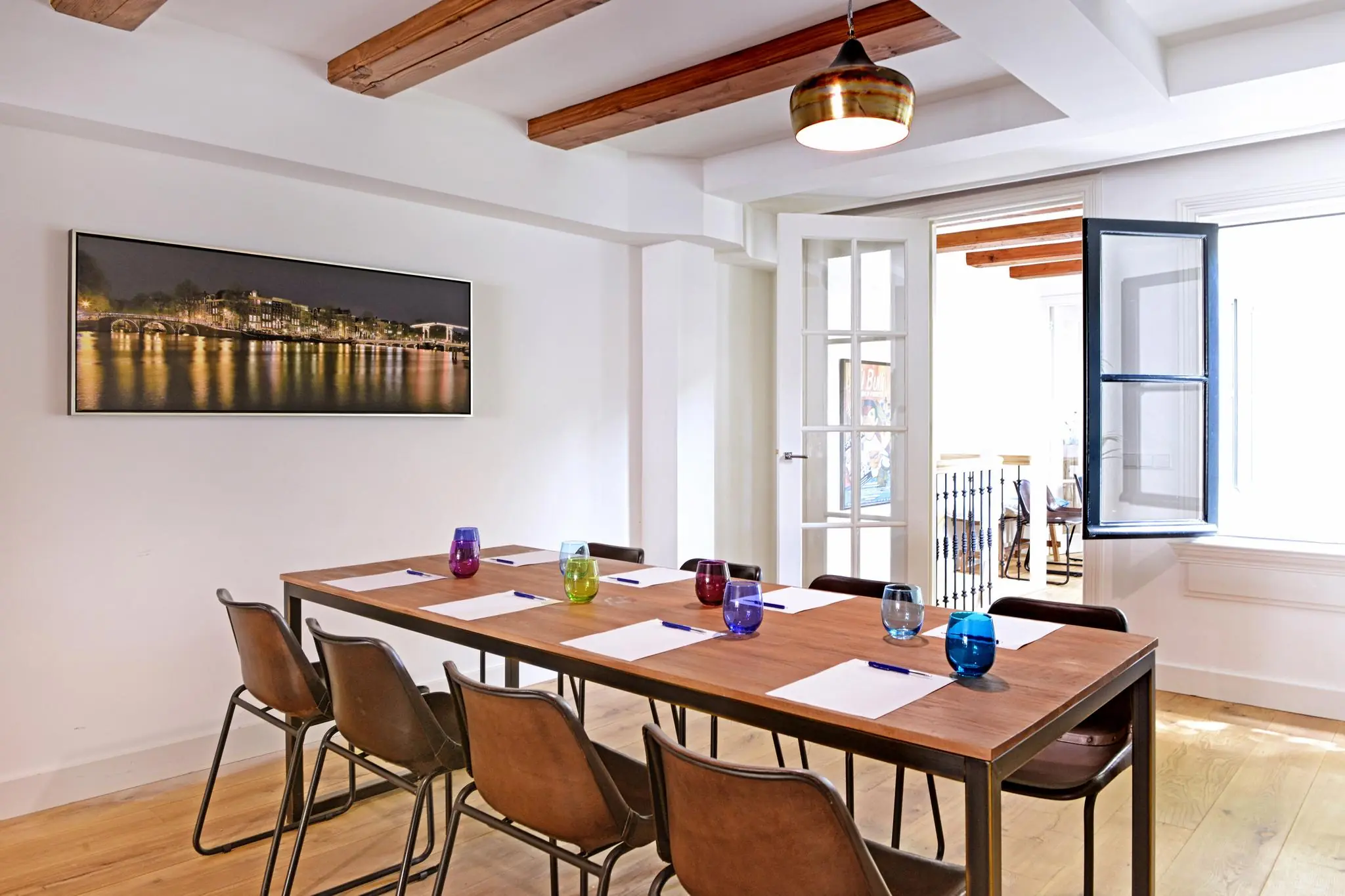 Vergaderruimte met houten tafel, leren stoelen, kleurrijke glazen en een groot raam in de Nieuwe Kerkstraat.